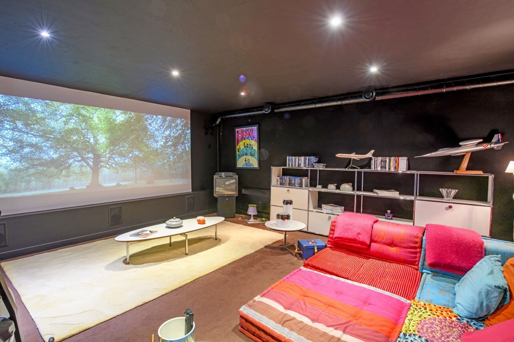 A modern living room with a large screen, a sofa, a coffee table, and a bookshelf.
