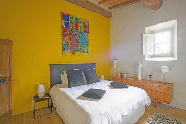 Un dormitorio con cama, cómoda, mesita de noche, un cuadro y una ventana.