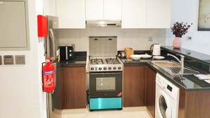 A modern kitchen with white cabinets, a stainless steel stove, a washing machine, and a fire extinguisher. - Beautiful Studio with balcony in JVC (Dubai)