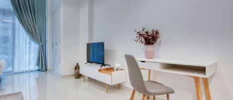 Un saló modern amb un televisor de pantalla plana, una taula de consola blanca, una cadira gris i un ram d'flors seques.