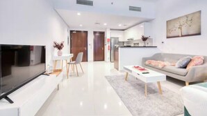 A modern living room with a flat-screen TV, a dining area with a table and chairs, a sofa with cushions, and a kitchen area in the background. - Beautiful Studio with balcony in JVC (Dubai)