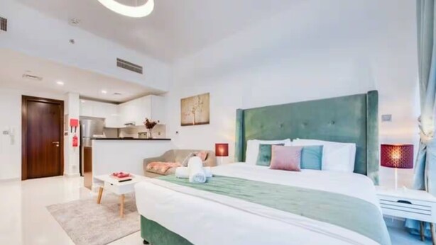 A modern hotel room with a large bed, a kitchenette, a seating area, and a bathroom. - Beautiful Studio with balcony in JVC (Dubai)