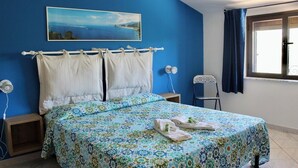A bedroom with a bed, a nightstand, a chair, a window with curtains, and a painting on the wall. - "House Kalavriya" 50mt from the sea (Nicotera Marina)