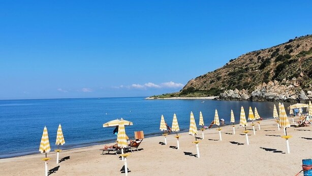 A beach with rows of yellow and white striped umbrellas and lounge chairs. - "House Kalavriya" 50mt from the sea (Nicotera Marina)