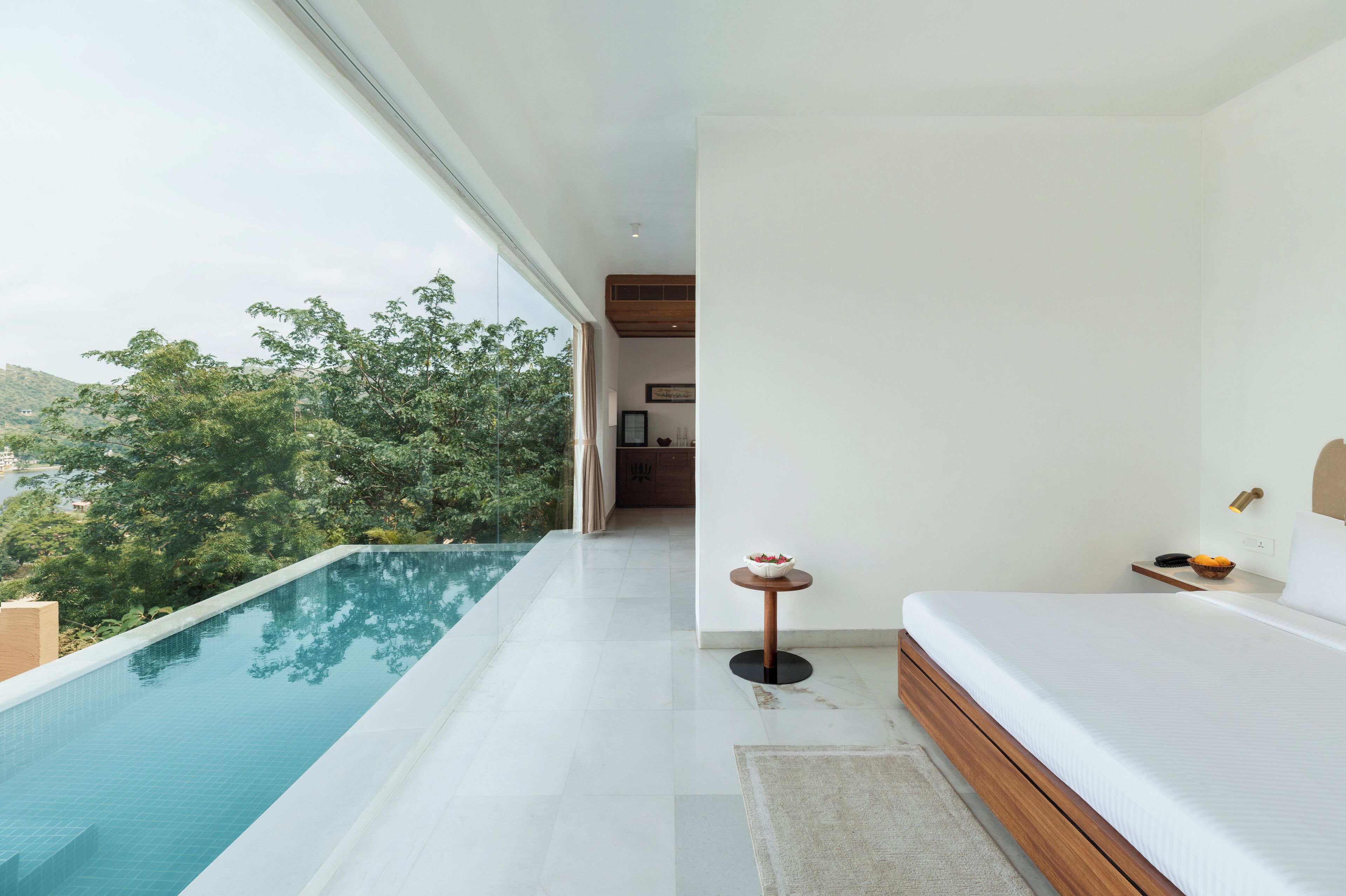 Ein modernes Schlafzimmer mit großem Fenster mit Blick auf einen Pool und üppige Bepflanzung.