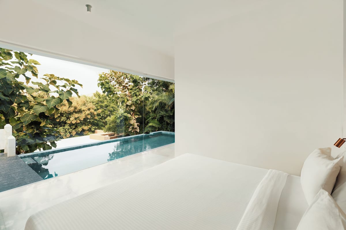Un dormitorio con un amplio ventanal que da a una piscina y abundante vegetación.