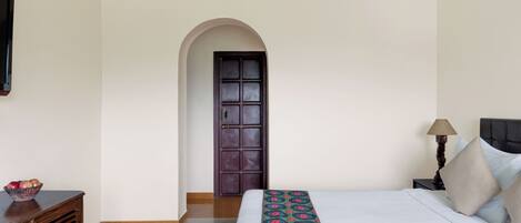 A hotel room with a bed, a nightstand, a lamp, a bowl of fruit, and a door.