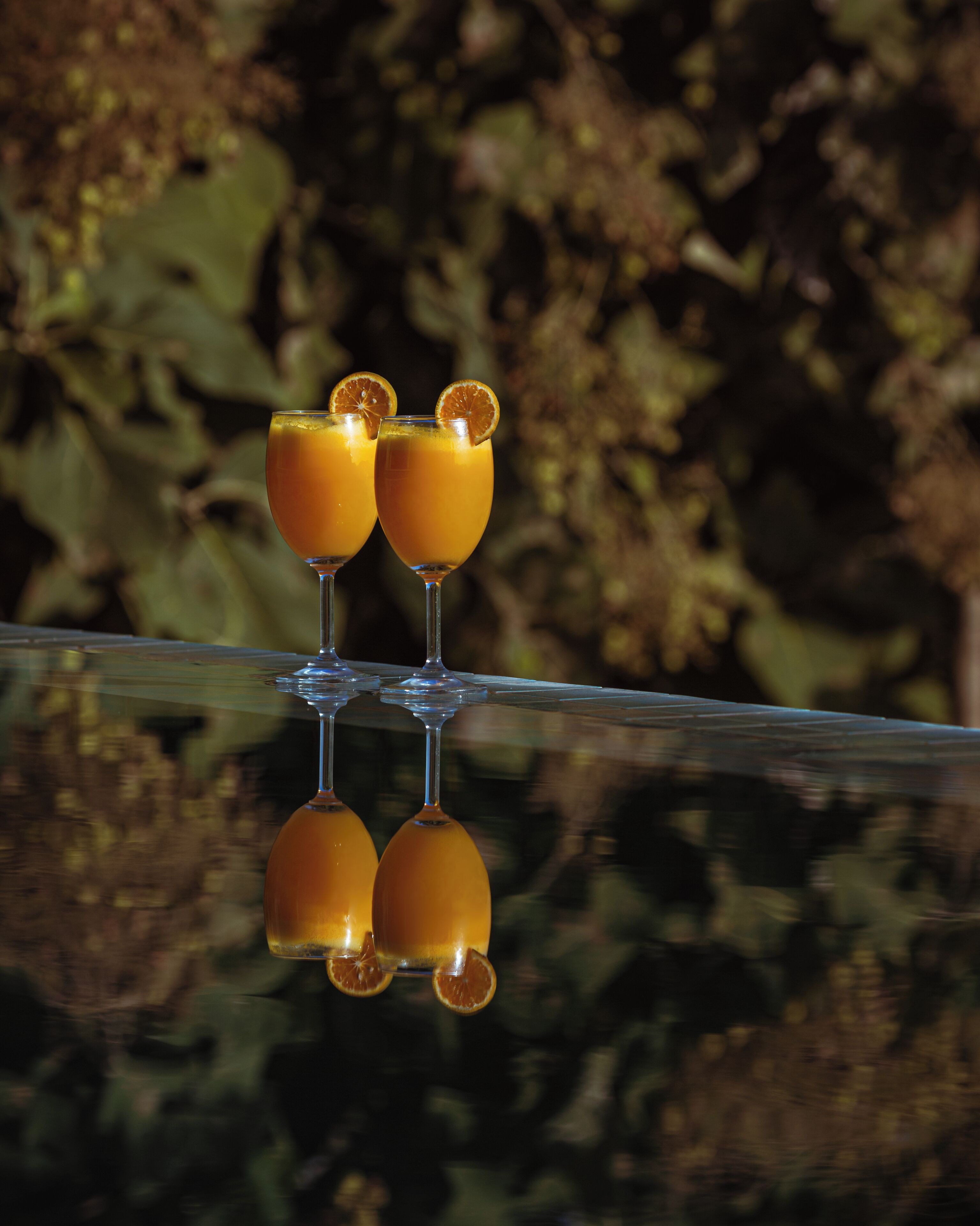 Three glasses of orange juice with orange slices on a reflective surface.