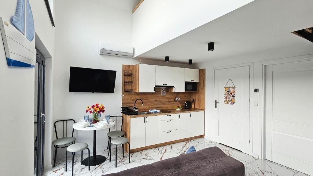 A compact kitchen with white cabinets, a microwave, and a sink. There's a dining area with a table and chairs, and a gray sofa.