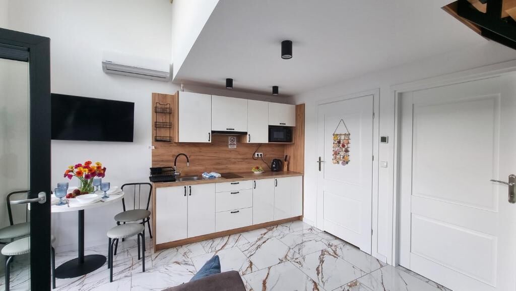 A compact kitchen with white cabinets, a microwave, and a wooden countertop. There is a dining area with a table and chairs, and a TV mounted on the wall.