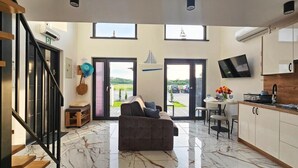 A modern living room with a sofa, a dining area with a table and chairs, and a kitchen with cabinets and a TV.