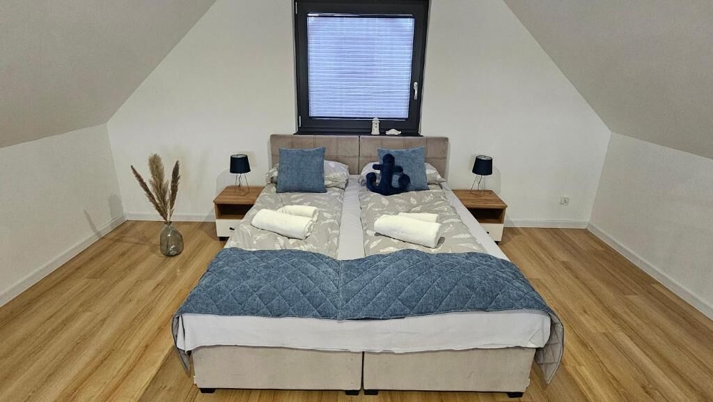 A bedroom with a large bed, two bedside tables, a window, and a vase with pampas grass.