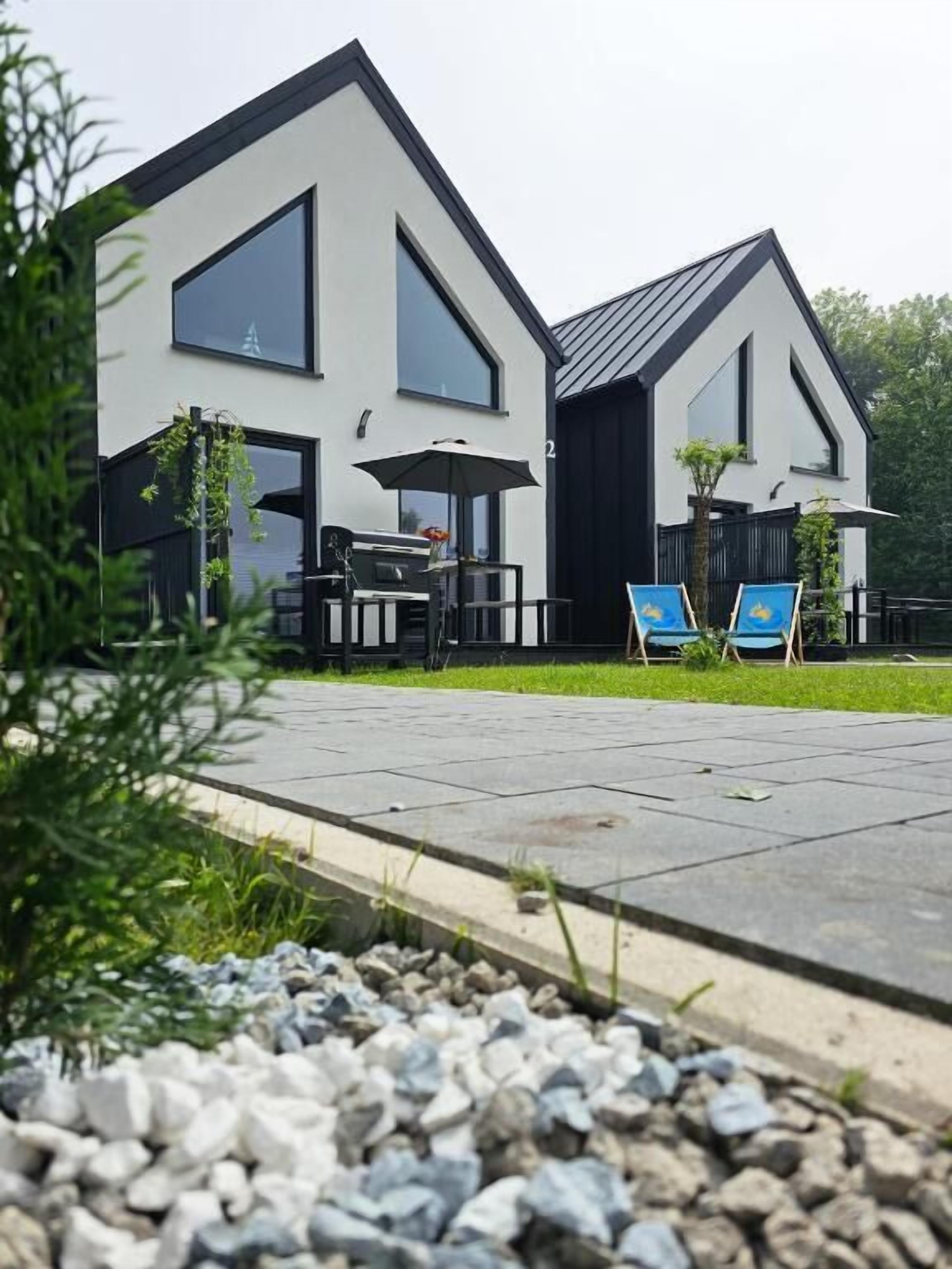 Egy modern, kétszintes ház terasszal, ahol grillező és kültéri ülőhely található.