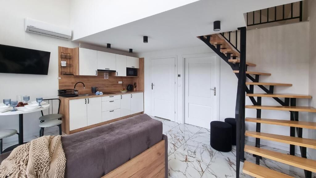 Une cuisine moderne avec des meubles blancs, un plan de travail en bois et un escalier noir.