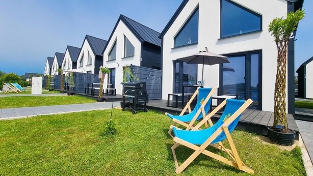 A row of modern, white houses with dark roofs, each featuring large windows and a small patio area.