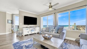 A spacious living room with a large TV, a comfortable sofa, and a view of the beach. - Sapphire Shores - Beachfront With Chair Setup (Panama City Beach)