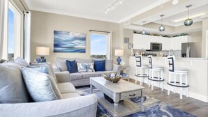 A modern living room with a sofa, coffee table, and a view of the kitchen. - Sapphire Shores - Beachfront With Chair Setup (Panama City Beach)