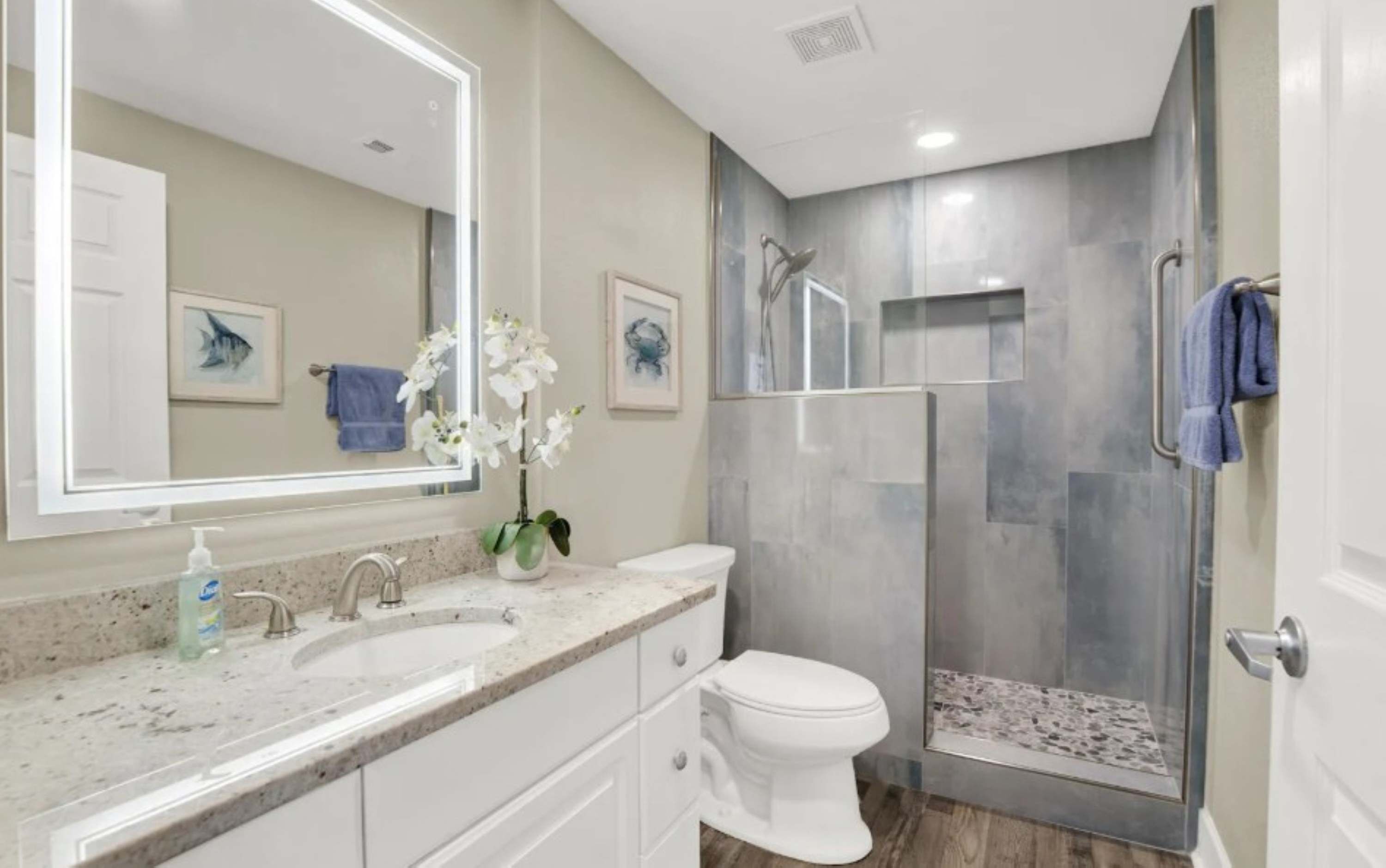 A modern bathroom with a large mirror, two sinks, a toilet, and a walk-in shower.