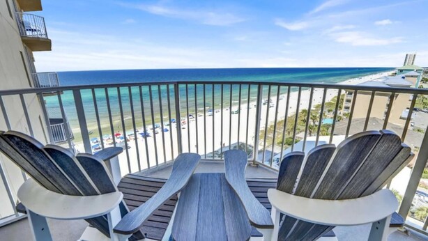 A balcony with two Adirondack chairs and a small table, overlooking a beach and ocean. - Sapphire Shores - Beachfront With Chair Setup (Panama City Beach)