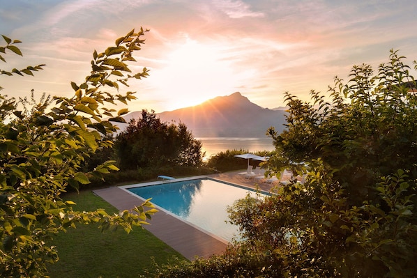 A swimming pool with a view of a mountain and a body of water at sunset.