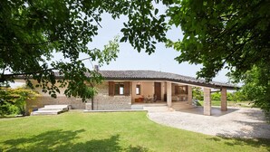 A stone house with a tiled roof, a covered patio, and a well-maintained lawn.