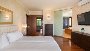 A bedroom with a large bed, a dresser, a TV mounted on the wall, and a bathroom visible through an open door.