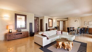 A spacious living room with a white sofa, glass coffee table, and a dining area with chairs and a table.