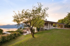 A modern house with a stone facade, a covered porch, and a view of a lake.