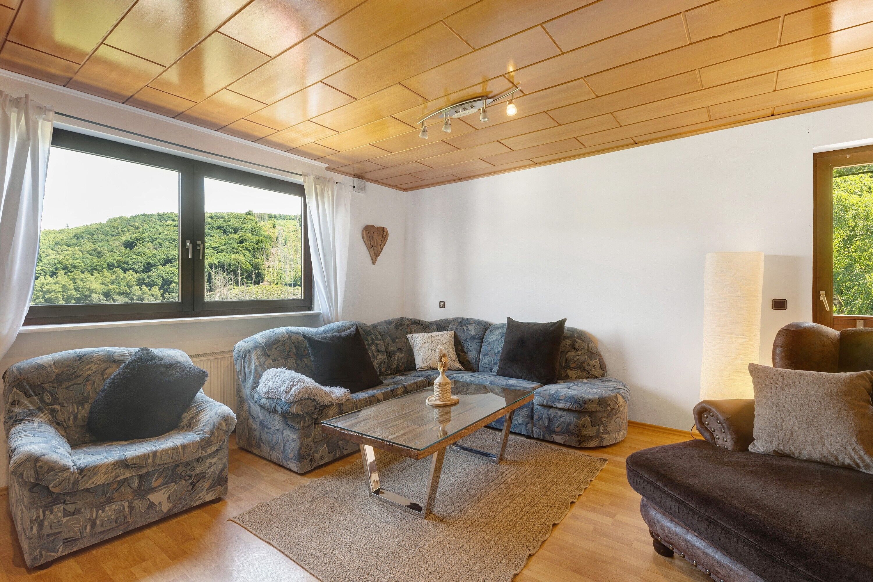 A living room with a wooden ceiling, a large window, two patterned sofas, a coffee table, and a rug.