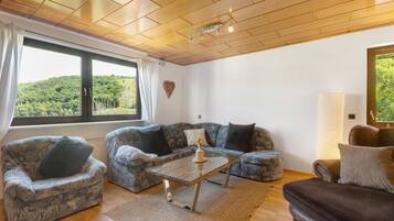 Ein Wohnzimmer mit Holzboden, einem großen Fenster, zwei gemusterten Sofas, einem Couchtisch und einem Teppich.