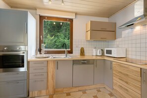 A modern kitchen with a built-in oven, a microwave, and a window with a view of trees. - Apartment 'Wohung Zum Ausblick' with Mountain View, Balcony and Wi-Fi (Plettenberg)