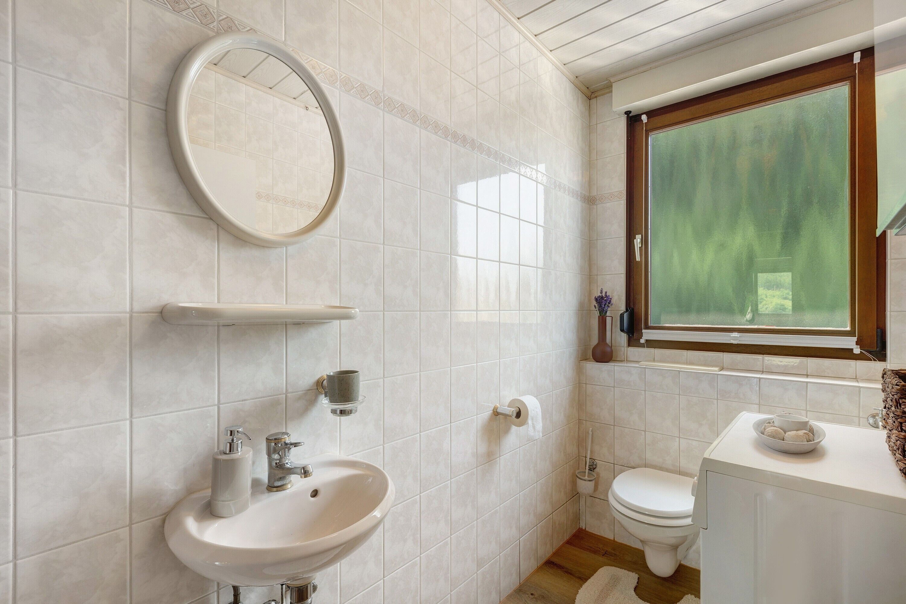Een badkamer met een wastafel, spiegel, toilet en raam met uitzicht.