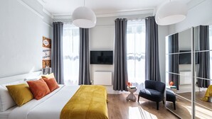 Una habitación de hotel moderna con una cama grande, un sofá, una silla, una mesita y un espejo amplio.