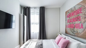 A hotel room with a bed, a flat-screen TV mounted on the wall, and a motivational poster.