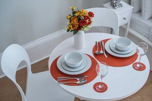 A dining table set with white plates, red placemats, and a vase of yellow and red flowers. - The Hideaway - Notting Hill Charming Studio (Greater London)