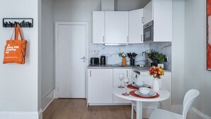 A compact kitchen with white cabinets, a countertop, and a dining area with a table set for two. - The Hideaway - Notting Hill Charming Studio (Greater London)
