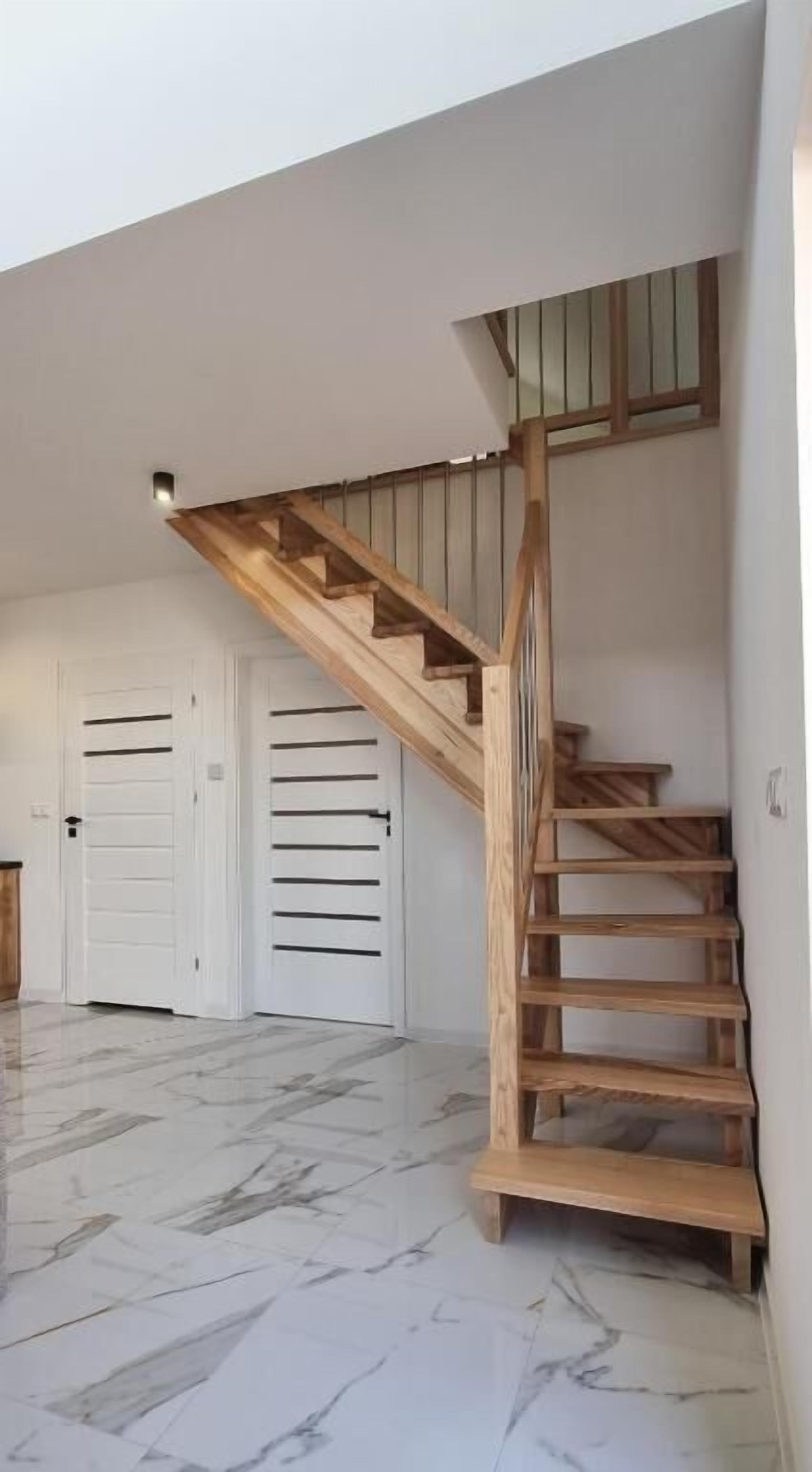 Ein geräumiges Zimmer mit Marmorboden, einer Holztreppe und weißen Türen mit horizontalen Lamellen.