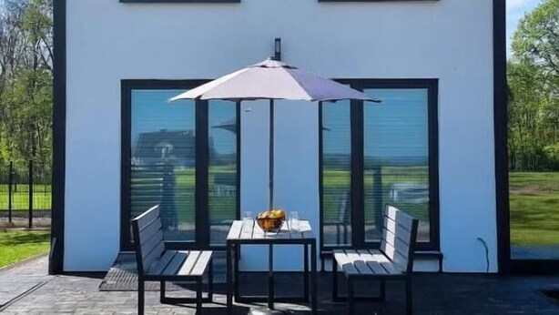 A modern two-story house with large windows and a patio area with a table and chairs. - ZATOR Domki INTERSTYL (Zator)