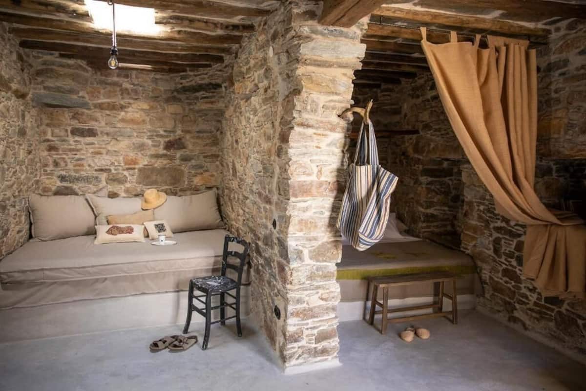 A rustic stone room with a sofa, a hanging chair, and a bench.