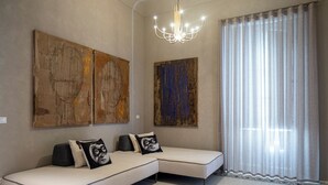 Ein modernes Wohnzimmer mit Ecksofa, abstrakter Wandkunst, einem Chandelier und einem großen Fenster mit transparenten Vorhängen.