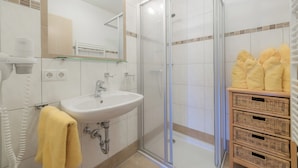 A bathroom with a glass shower enclosure, a sink, and a mirror. There are towels hanging on the wall and baskets of towels on a shelf. - The apartments are located in a quiet and central area—ideal for families (Flachau)