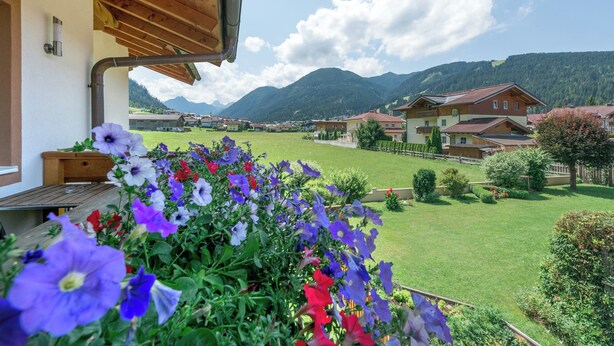 A balcony with a wooden railing overlooking a green lawn and a village with houses and mountains in the background. - The apartments are located in a quiet and central area—ideal for families (Flachau)
