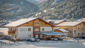 A snow-covered mountain resort with wooden buildings, a parking area, and a view of the mountains. - The apartments are located in a quiet and central area—ideal for families (Flachau)