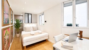 A modern bedroom with a bed, bedside table, laptop, and framed artwork. - 1548 GrosCaillou (Paris)