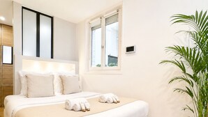 A hotel room with a bed, bedside table, window, and a potted plant. - 1548 GrosCaillou (Paris)