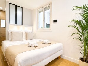 A hotel room with a bed, bedside table, window, and a potted plant. - 1548 GrosCaillou (Paris)