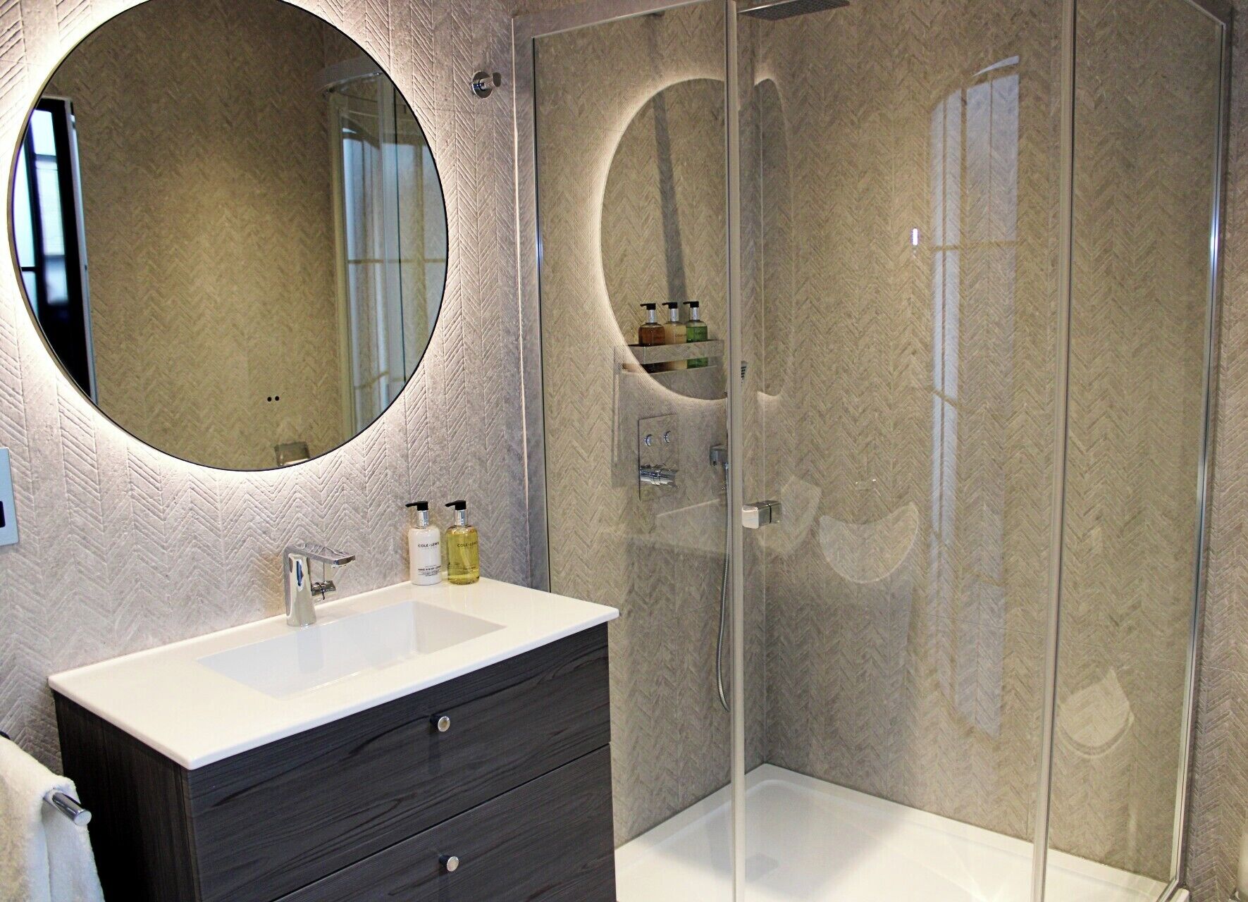 Un baño moderno con un espejo redondo grande, un lavabo blanco y un mueble de tocador de madera oscura.