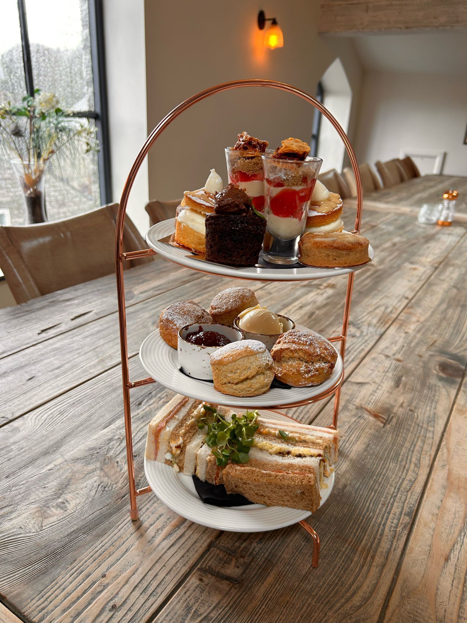 A three-tiered dessert stand with various pastries and desserts on a wooden table in a dining area.