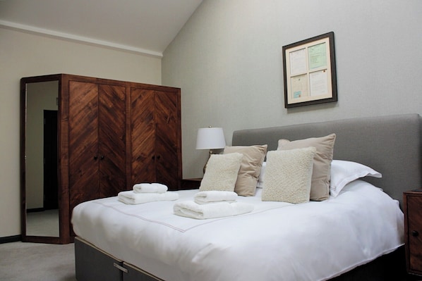 A neatly made bed with white linens and towels, a wooden wardrobe, a nightstand with a lamp, and a framed notice on the wall. - The Merchant's Yard (Tideswell)