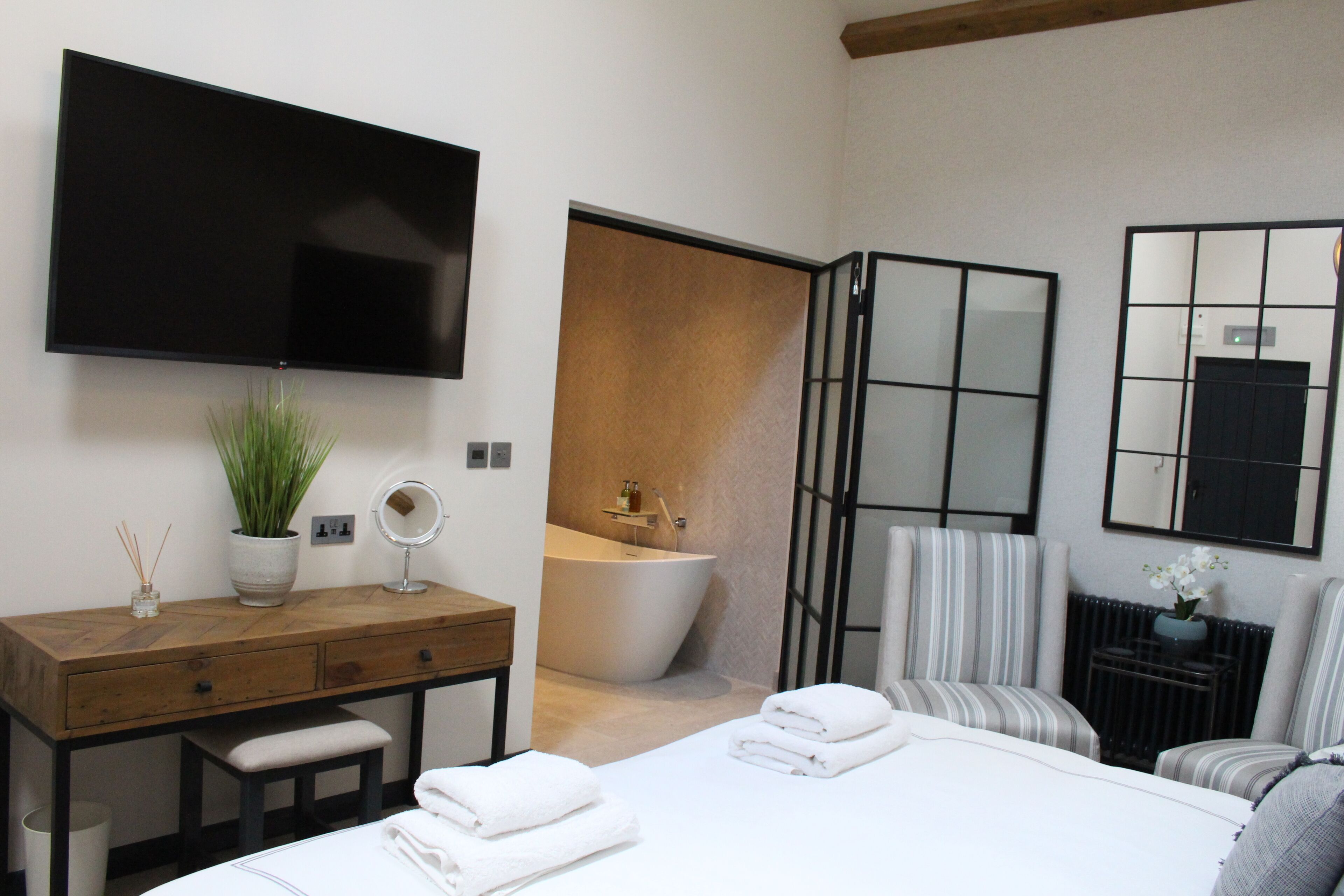A modern bedroom with a large bed, a wooden dresser, a flat-screen TV, a bathtub, and a mirror.